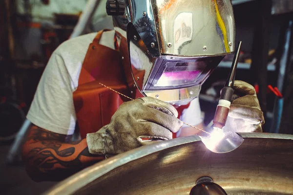 The man in the mask brews beautiful welds with argon-arc welding