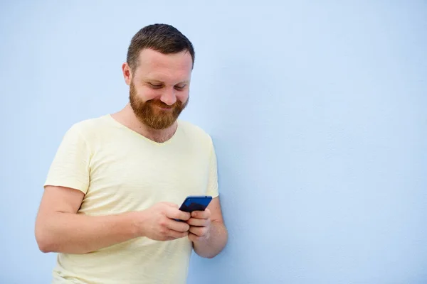 Veselý muž s červenou bradku vypadá do telefonu na modrém pozadí — Stock fotografie