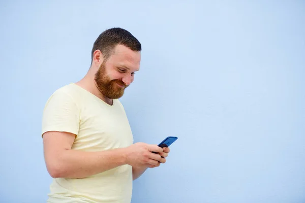 Veselý muž s červenou bradku vypadá do telefonu na modrém pozadí — Stock fotografie