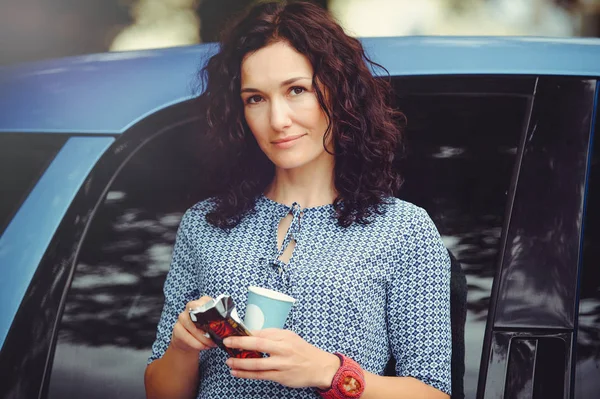 Gyönyörű göndör nő kávéfogyasztás közelében az autó a kék ruha — Stock Fotó