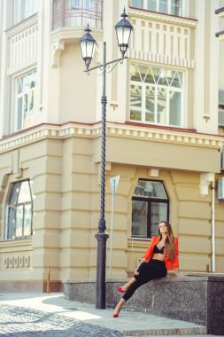 Tatlı bir yüzü bir muamma. Mutlu bir kadın kırmızı tarzı ceket ve siyah pantolon moda portre yeni ev, yeni bir bina arka plan üzerinde oturur. banner ve reklam için yer