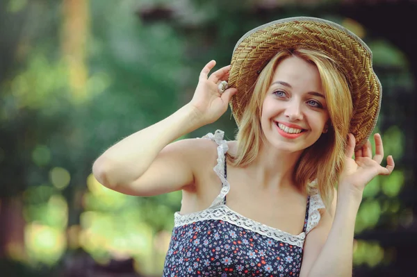 一个健康的女人美丽夏日模特女孩带着鲜艳的花朵快乐的森林。风格休闲。一个漂亮的白女人戴着草帽一个微笑和神秘的漂亮的脸。横幅和广告的地方 — 图库照片