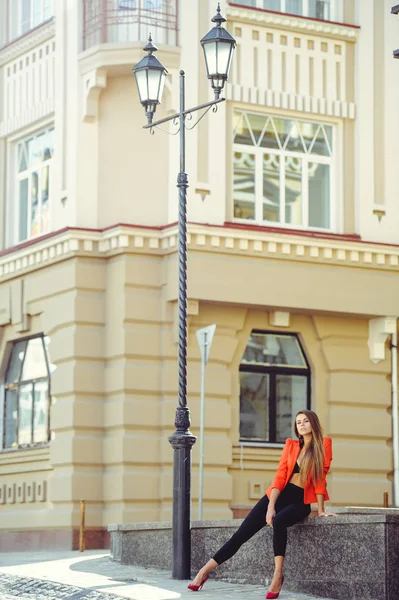 Um rosto doce é um mistério. Retrato de moda de uma mulher feliz em jaqueta de estilo vermelho e calças pretas fica no fundo de novas casas, um novo edifício. lugar para banner e publicidade — Fotografia de Stock