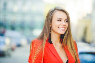 Şık bir görünüm, şehirde, açık havada şehir sıcak arka plan üzerinde kırmızı bir ceket, sarı saçlı ve bir gülümseme giyen sıcak gün modeli genç bir kadın yürüyor