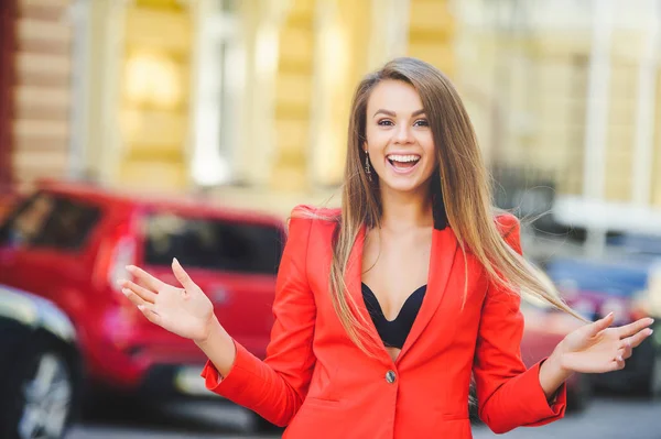Модная внешность, в жаркий день модель молодой женщины разгуливает по городу в красной куртке, волосах и улыбке на теплом фоне города — стоковое фото