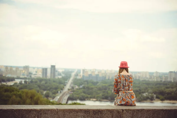 Mädchen in Kleid und Hut blickt aus der Höhe auf die Stadt — Stockfoto