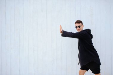 şık adam beyaz bir duvar. Yükseltir ellerini çerçevenin sol tarafında duruyor. beyaz gömlek ve siyah şort giymiş. sol tarafı metin için