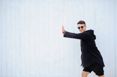 şık adam beyaz bir duvar. Yükseltir ellerini çerçevenin sol tarafında duruyor. beyaz gömlek ve siyah şort giymiş. sol tarafı metin için