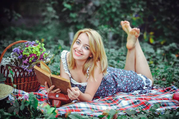 Schöne junge Frau beim Picknick auf dem Land. glücklicher gemütlicher Tag im Freien. Offen. Lächelnde Frau mit Buch in der Hand, entspannt im Park. Erholung — Stockfoto