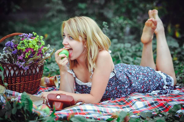 Mooie jonge vrouw met een picknick in het platteland. Gelukkig, gezellige dag in de buitenlucht. Open. Lachende vrouw eten apple, ontspannen in het park. rust en gezondheid — Stockfoto