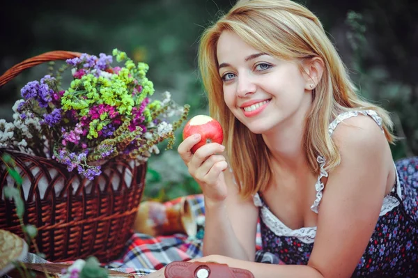 Hermosa joven haciendo un picnic en el campo. Feliz día al aire libre. Abran. Mujer sonriente comiendo manzana, relajándose en el parque. descanso y salud — Foto de Stock