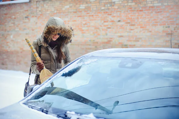 Glückliches Mädchen, das in der Stadt sein Auto vom Schnee befreit. beim Hausbesen — Stockfoto