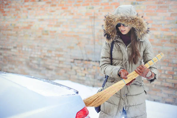 Szczęśliwa dziewczyna czyszczenie jej samochodu ze śniegu w mieście. Broom house — Zdjęcie stockowe