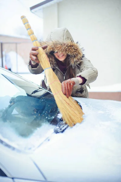 Счастливая девушка убирает свою машину со снега в городе. Рядом с метлой — стоковое фото