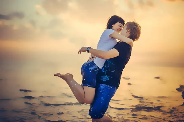 O casal está se beijando ao pôr do sol contra o fundo do mar, a menina em seus braços dobrou as pernas, um desenho quente, um lugar para texto e publicidade — Fotografia de Stock