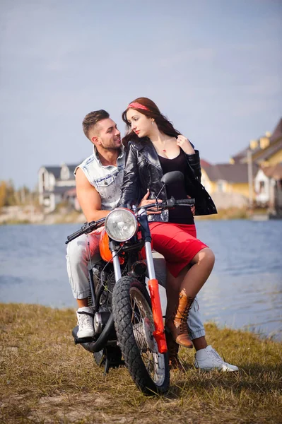 stylish and trendy couple in love on a motorcycle flirting close-up on a background of late autumn in the park