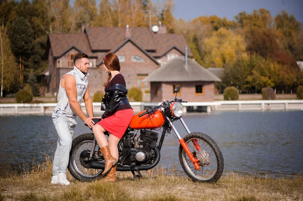 Elegante e moderno casal apaixonado em uma motocicleta flertando close-up em um fundo do final do outono no parque — Fotografia de Stock