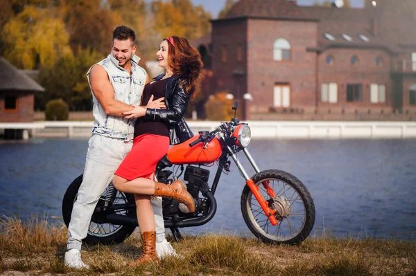 stylish and trendy couple in love on a motorcycle flirting close-up on a background of late autumn in the park