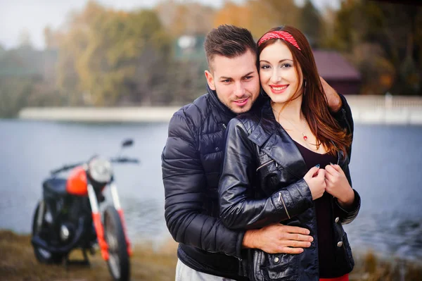 Pareja elegante y de moda en el amor en una motocicleta coqueteando primer plano en un fondo de finales de otoño en el parque — Foto de Stock