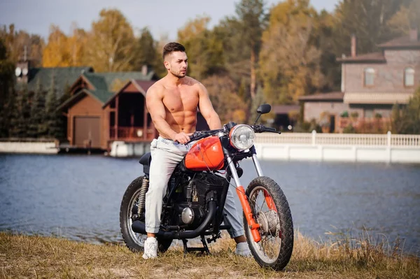 Young sports fashionable man with a naked torso, fitness coach on a motorcycle, a warm shot, late autumn — Stock Photo, Image