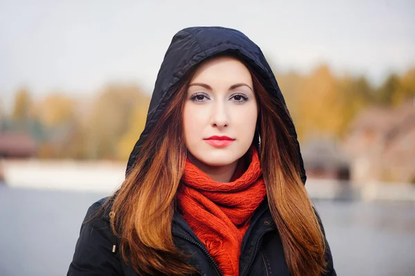 Joven mujer bonita en una capucha en la estación fría contra un bosque amarillo, pelo rojo y una bufanda alrededor de su cuello — Foto de Stock