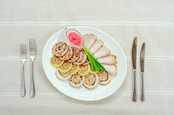 sliced delicious meat rolls on a white plate with horseradish and spring onion, restaurant serve, table setting