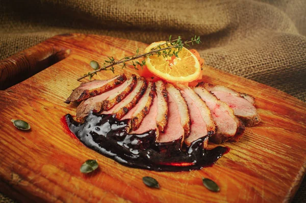 Duck fillet on a wooden surface with black sauce and orange, rosemary and carrots, cozy table setting, restaurant serve — Stock Photo, Image