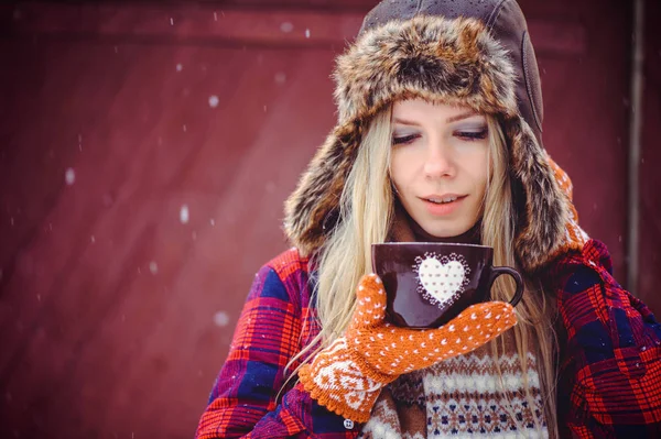 Sanfte Frau mit Wintermütze und Vareks mit einer Tasse heißem Tee oder Kaffee auf rotem Hintergrund, ein heller Werbefilm — Stockfoto