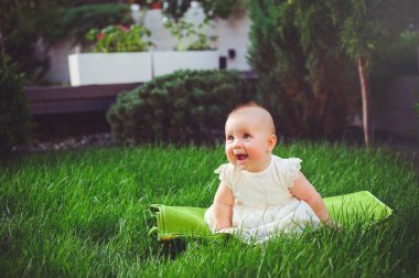 Beyaz bir elbise giymiş bahçedeki çimlerin üzerine oturan yarı yaşındaki çocuk, 6 ay sevinir. Çocukların, çocuk mal kavram eğitimi