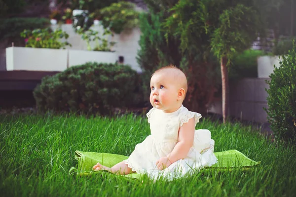 Half-jaar oude kind zittend op het gras in de tuin, gekleed in een witte jurk verheugt zich, 6 maanden. Concept onderwijs voor kinderen, kinderen van goederen — Stockfoto