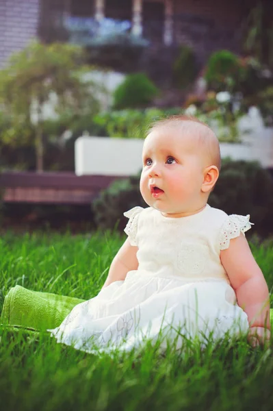 Half-jaar oude kind zittend op het gras in de tuin, gekleed in een witte jurk verheugt zich, 6 maanden. Concept onderwijs voor kinderen, kinderen van goederen — Stockfoto