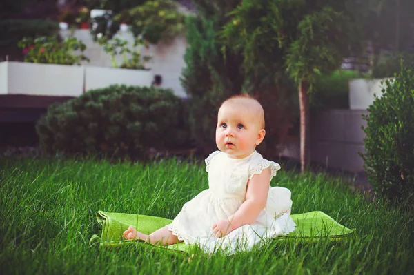 Halvt-åriga barn sitter på gräset i gården, klädd i en vit klänning jublar, 6 månader. Begreppet utbildning av barn, barns varor — Stockfoto