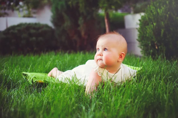 Niño de medio año se arrastra sobre la hierba en el patio, vestido con un vestido blanco se regocija, 6 meses. Concepto educación de los niños, bienes de los niños —  Fotos de Stock