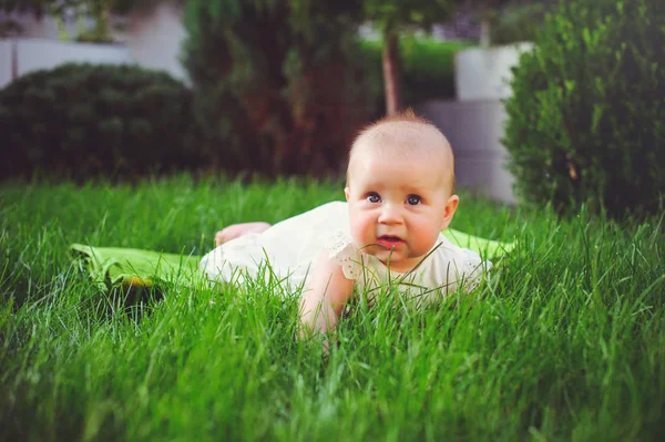 Niño de medio año se arrastra sobre la hierba en el patio, vestido con un vestido blanco se regocija, 6 meses. Concepto educación de los niños, bienes de los niños —  Fotos de Stock