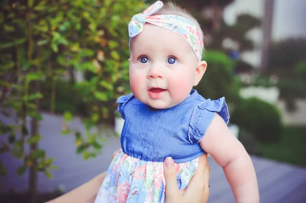 Porträtt av ett sex månader gammalt barn jublar, är klädd i en blå klänning och ett bandage på huvudet, 6 månader gamla mor har på händerna. Begreppet utbildning av barn, barns varor — Stockfoto