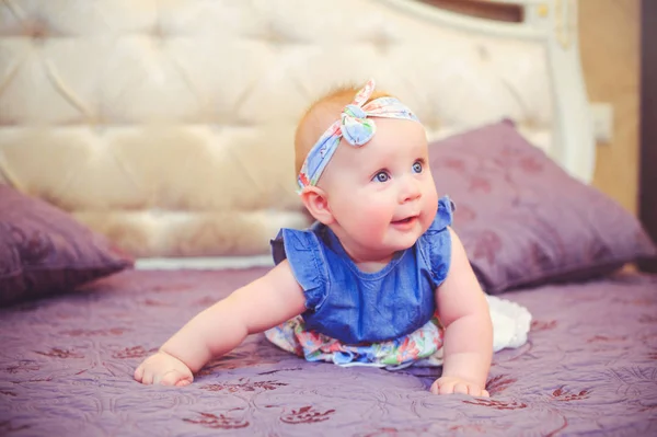 Porträtt av ett halvt-åriga barn liggande på sängen är glad, klädd i en blå klänning och ett bandage på huvudet, 6 månader gammal med sin mor i hennes armar. Begreppet utbildning av barn, barns varor — Stockfoto