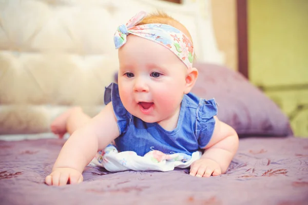 Porträtt av ett halvt-åriga barn liggande på sängen är glad, klädd i en blå klänning och ett bandage på huvudet, 6 månader gammal med sin mor i hennes armar. Begreppet utbildning av barn, barns varor — Stockfoto