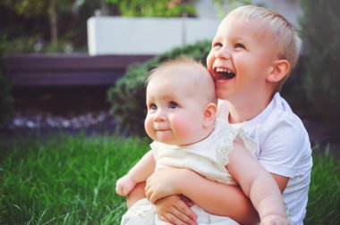 mutlu küçük kardeşim oynarken hugs kardeşi çim yeşil Bahçe, aşk ve ebeveynlik kavramı üzerinde oturan bebek