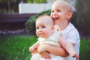 mutlu küçük kardeşim oynarken hugs kardeşi çim yeşil Bahçe, aşk ve ebeveynlik kavramı üzerinde oturan bebek