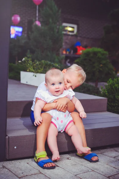 Heureux petit frère joue câlins sa soeur bébé, garçon et fille sont assis dans un jardin vert, le concept d'amour et de parentalité — Photo