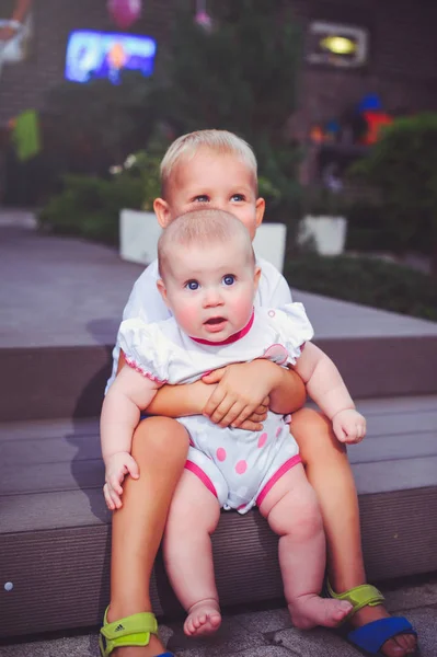 Heureux petit frère joue câlins sa soeur bébé, garçon et fille sont assis dans un jardin vert, le concept d'amour et de parentalité — Photo