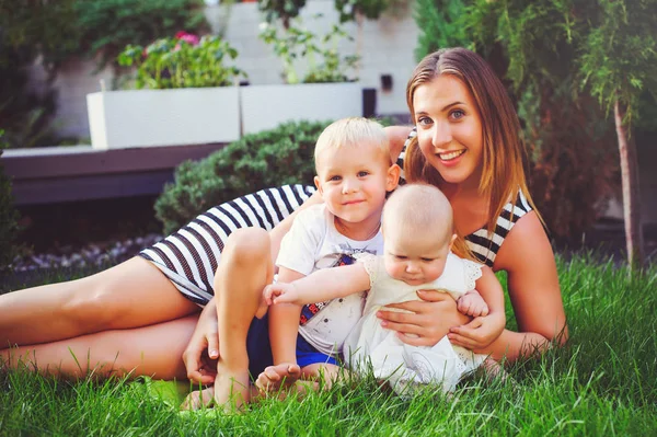 Femme mère avec deux jeunes enfants couché sur une pelouse verte, concept maternité et parentalité — Photo