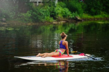 Genç atletik kadının bir tahta üzerinde Fitness bir göl kenarında birer kürek ile yapması