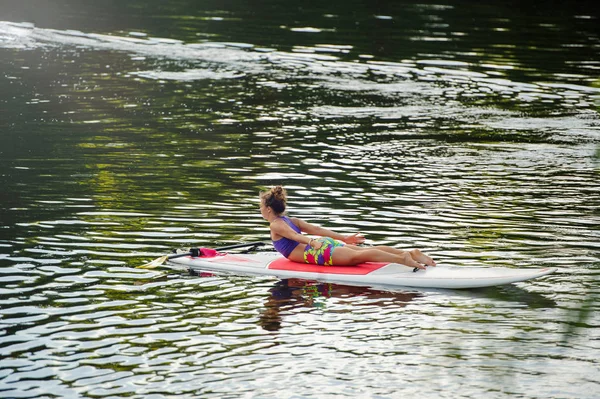 Junge athletische Frau beim Fitnesstraining auf einem Brett mit einem Ruder auf einem See — Stockfoto