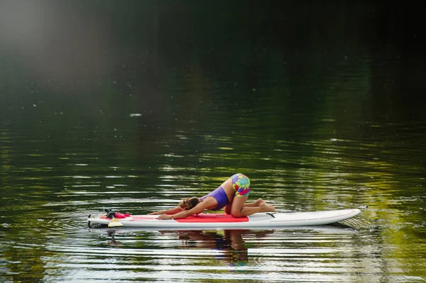 Junge athletische Frau beim Fitnesstraining auf einem Brett mit einem Ruder auf einem See — Stockfoto