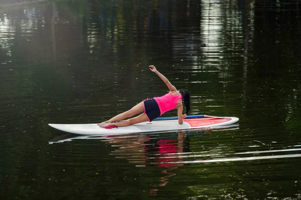 Junge athletische Frau beim Fitnesstraining auf einem Brett mit einem Ruder auf einem See — Stockfoto