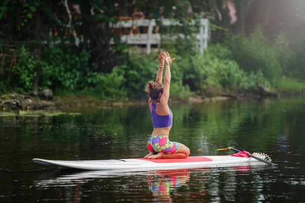 Young athletic woman doing fitness on a board with an oar on a lake — Stock Photo, Image