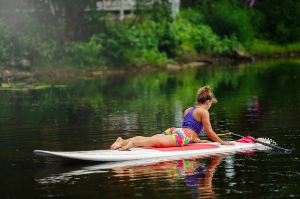 Junge athletische Frau beim Fitnesstraining auf einem Brett mit einem Ruder auf einem See — Stockfoto