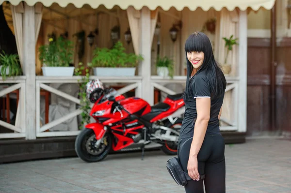 Девушка-байкер в черной одежде на спортивном мотоцикле позирует в городе — стоковое фото