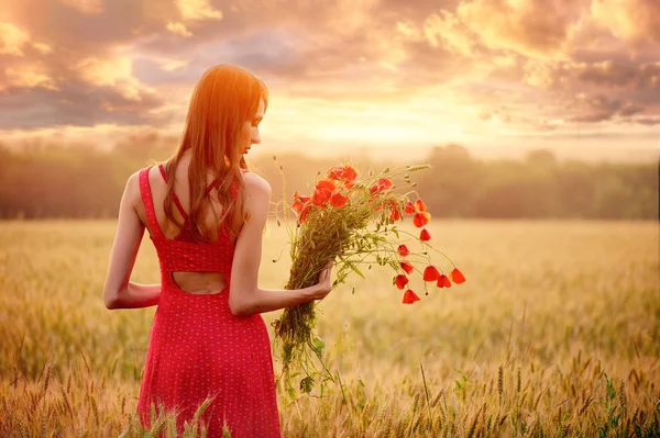 Hermosa mujer en un vestido rojo con un ramo de amapolas en un campo de trigo al atardecer, tonificación cálida, felicidad y un estilo de vida saludable —  Fotos de Stock